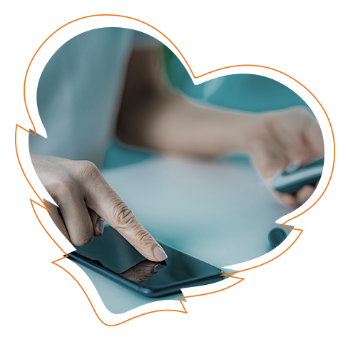 An image featuring a hand holding a smartphone over a tabletop, with a blurred background showing a person s hands on a tablet screen, suggesting technology use and interaction.