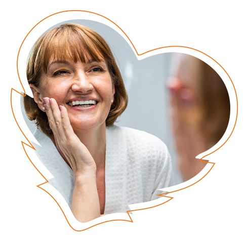 The image shows a woman with smiling eyes looking directly at the camera, wearing a white top and a heart-shaped sticker placed over her face. She has short hair and appears to be in a professional setting, possibly related to beauty or skincare services.