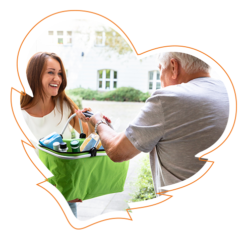 An elderly person handing a package to a younger individual who appears to be offering a card or gift with a smile, both standing on a porch.