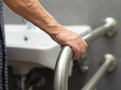 The image shows an elderly person holding onto a grab bar next to a sink in a bathroom setting.