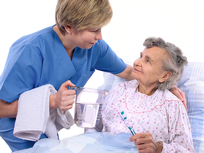 The image shows a female nurse attending to an elderly woman who appears to be in a hospital bed.