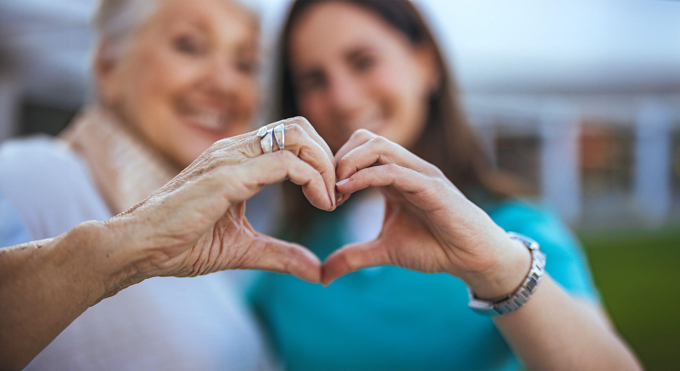 Two elderly individuals holding hands and forming a heart shape with their fingers.